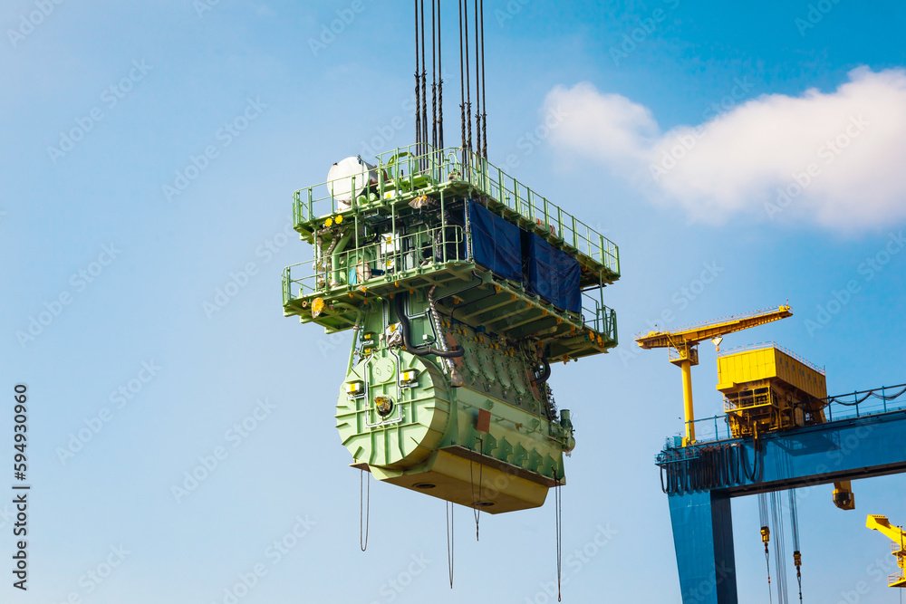 Transportation of a large marine engine by a port crane using steel cables.